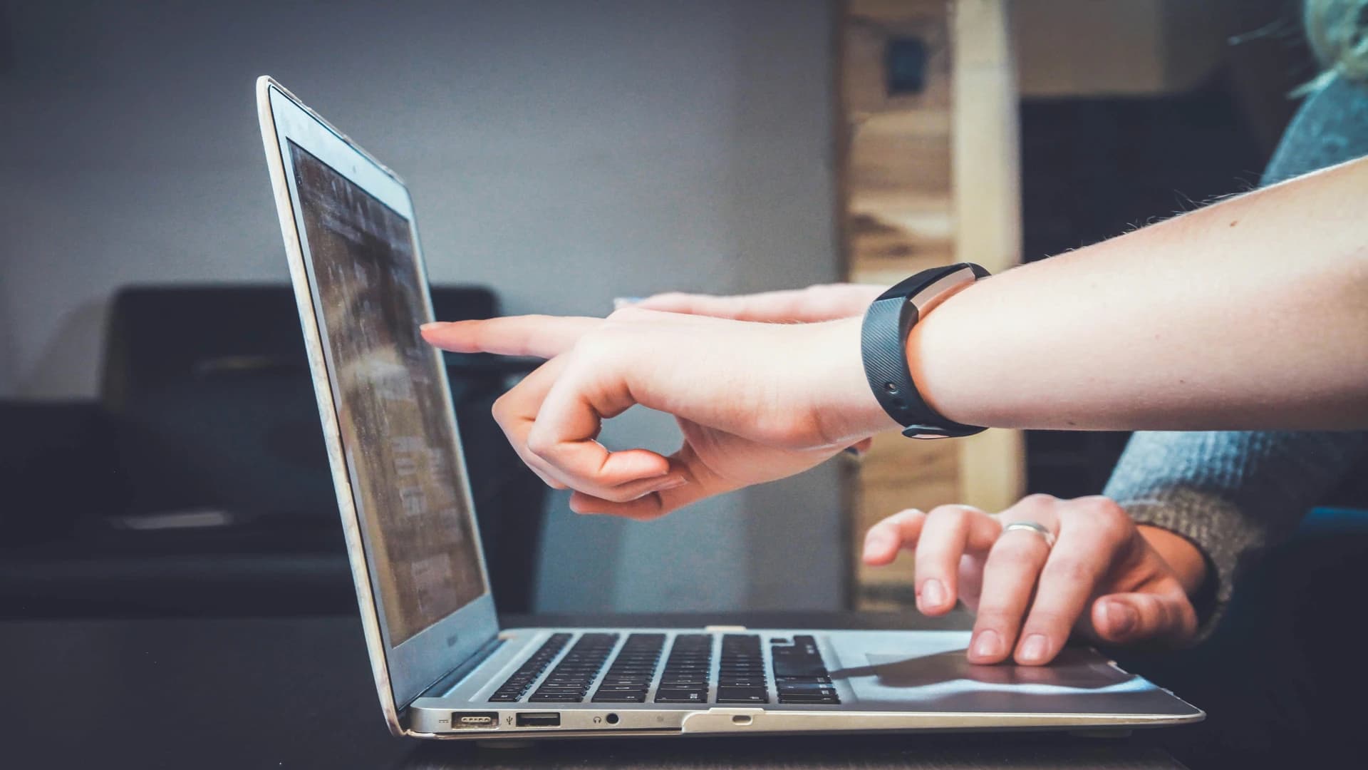 Two people pointing at a laptop screen while working together.