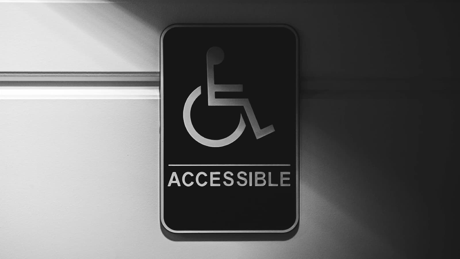 Black-and-white accessible entrance sign with a wheelchair symbol mounted on a wall.