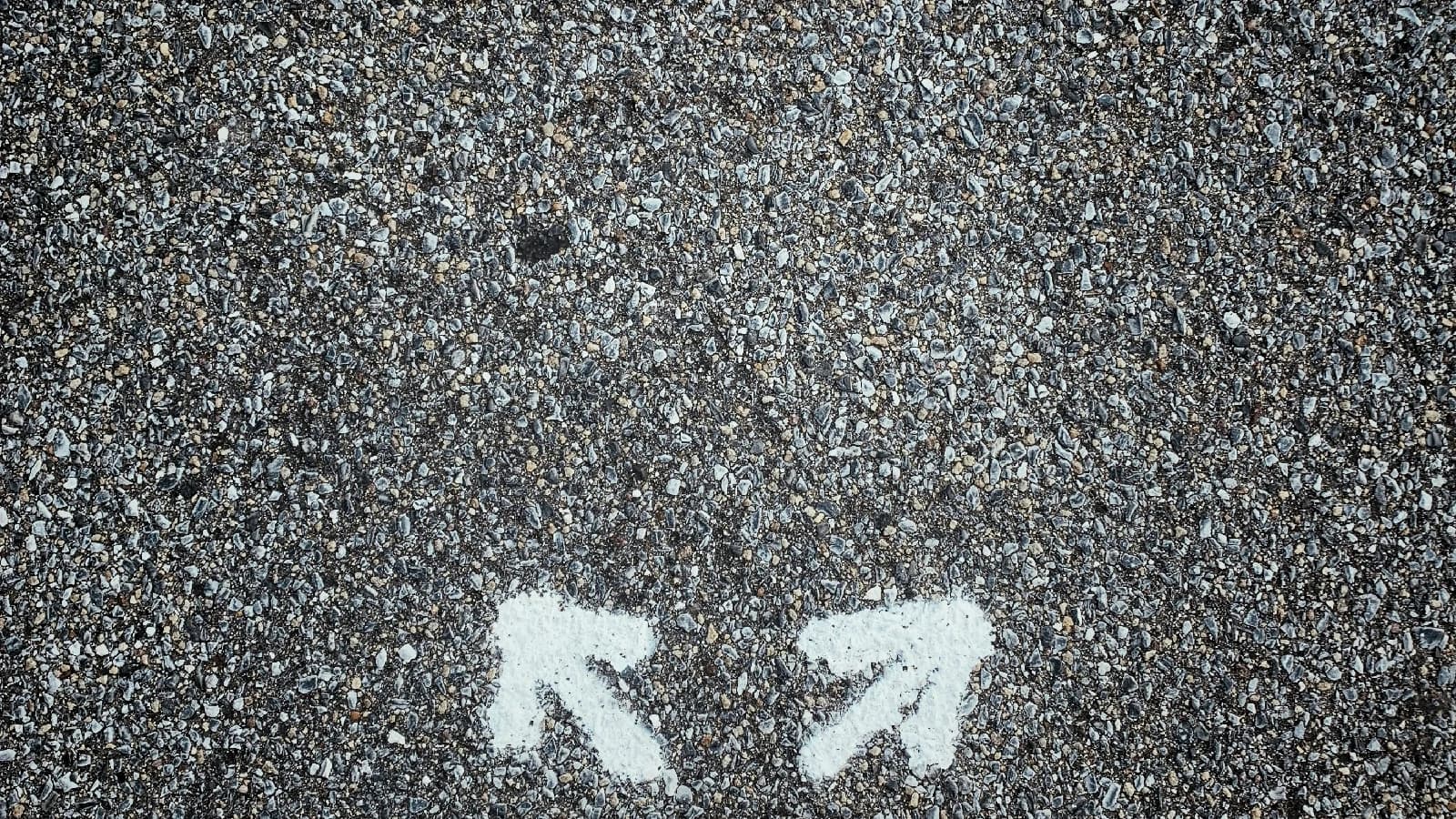 Two white arrows painted on gravel, pointing in opposite directions.
