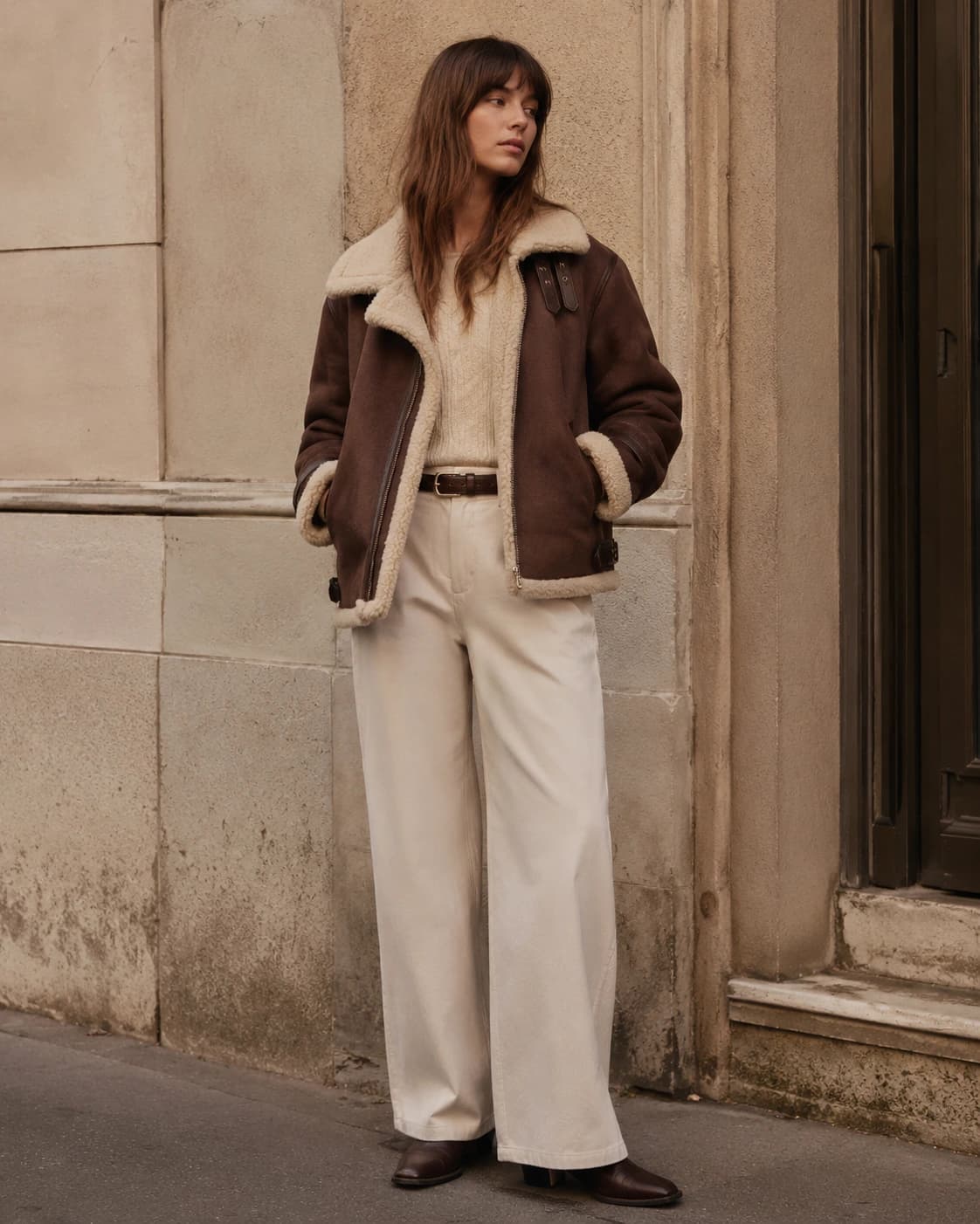 Woman wearing a brown shearling aviator jacket with cream wide-leg trousers
