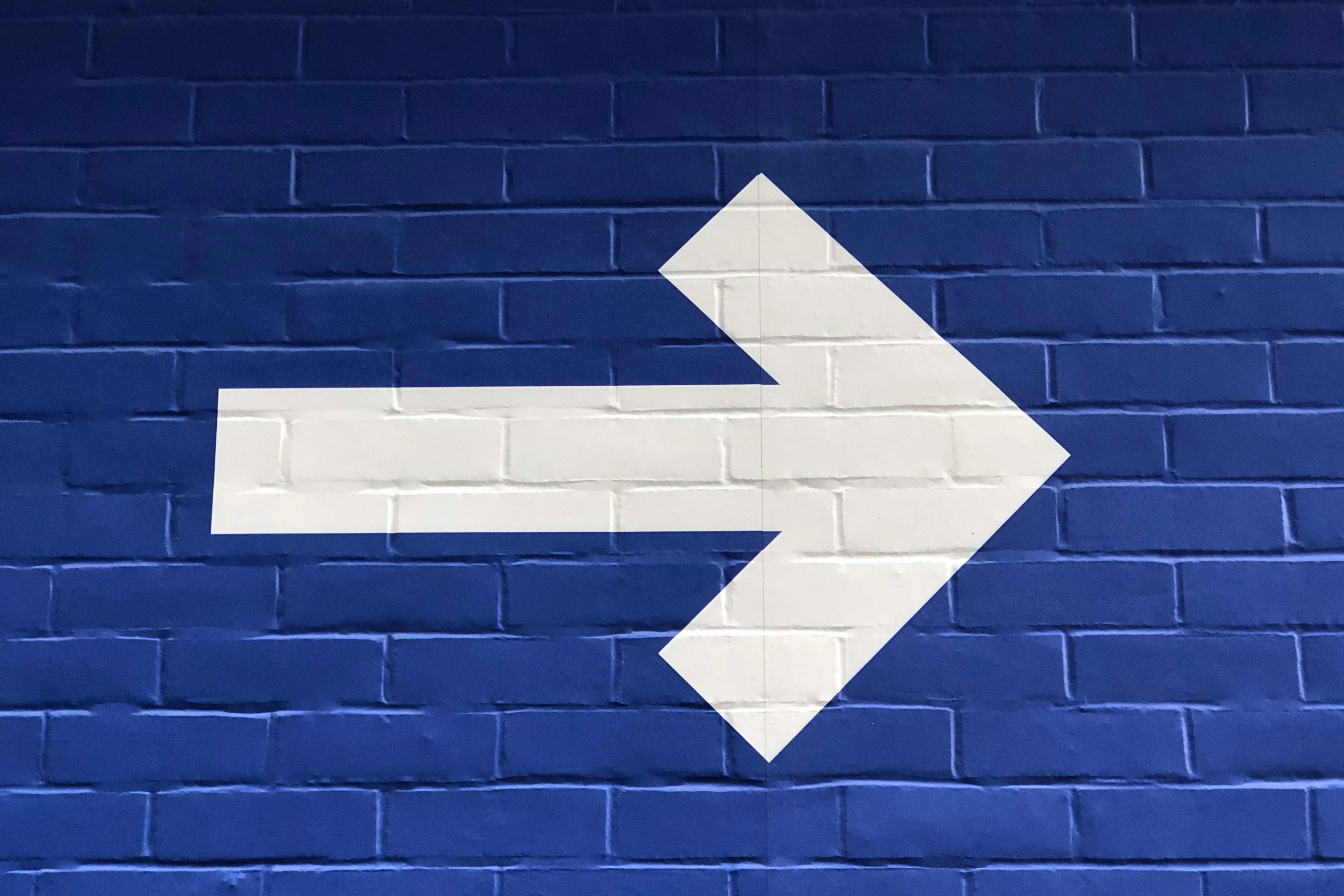 A large white arrow pointing right on a dark blue brick wall.