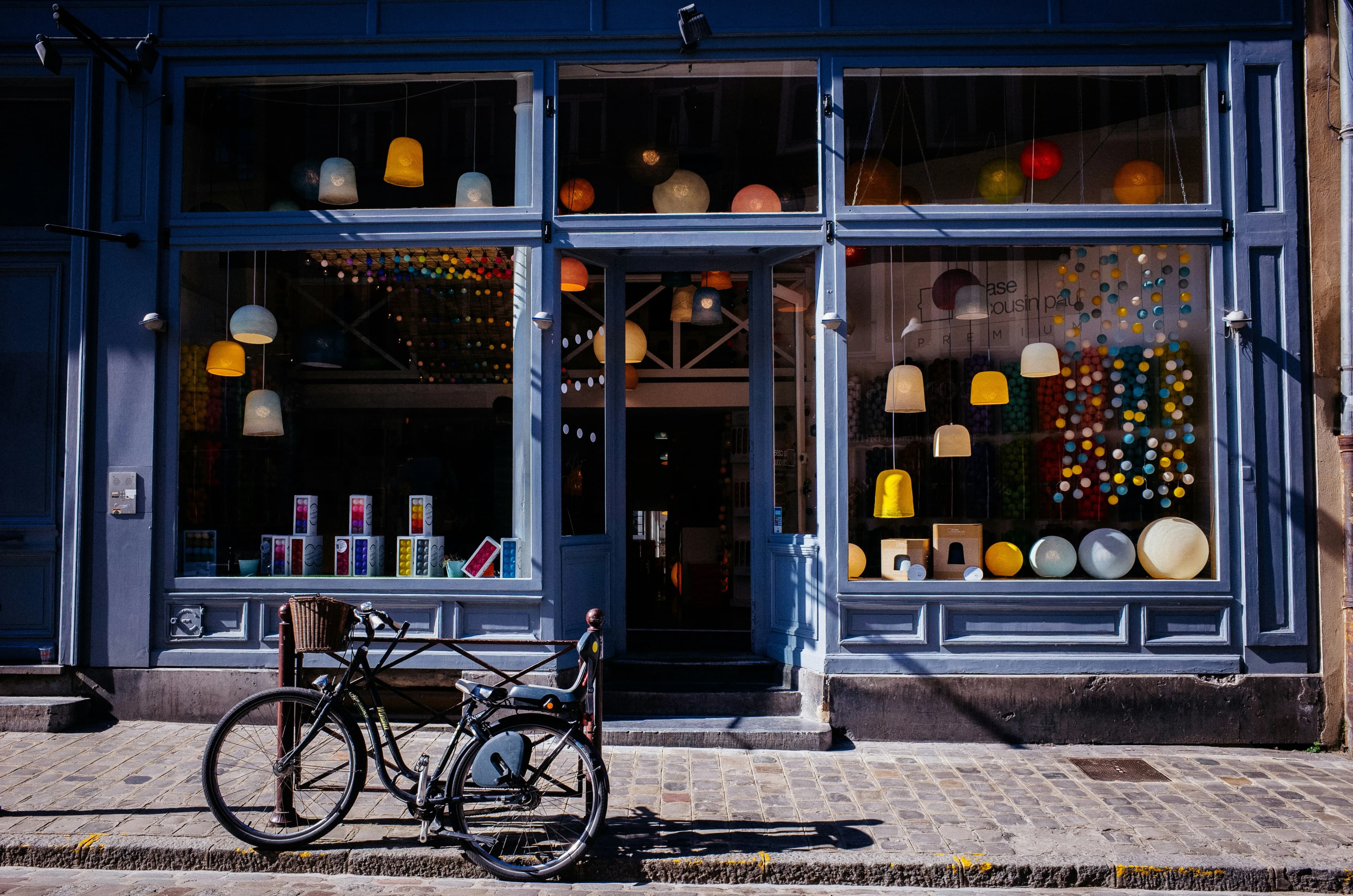 A blue-painted shopfront displaying colourful lamps, with two bicycles parked outside.