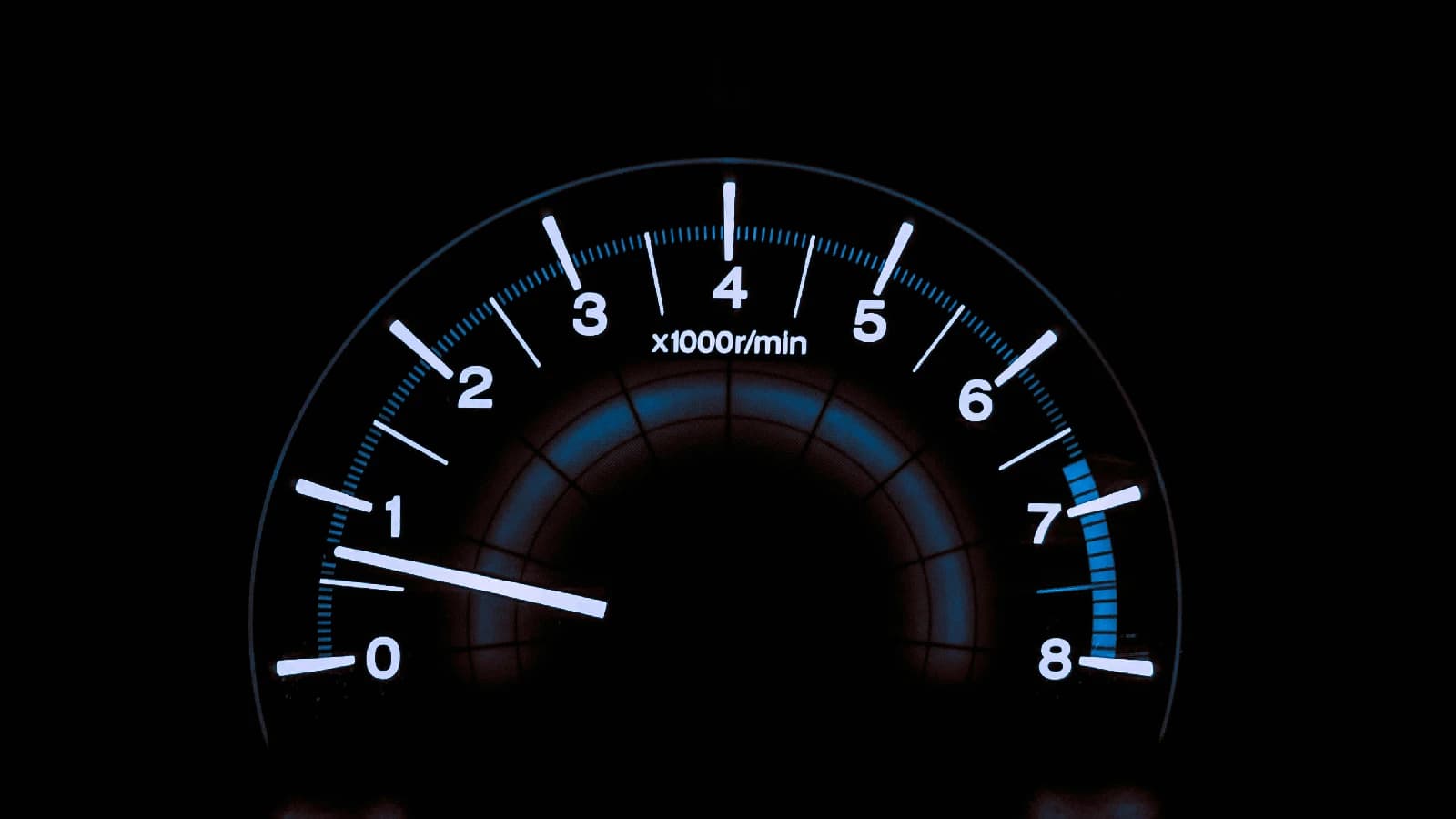 Illuminated car tachometer marked from zero to eight against a black background.